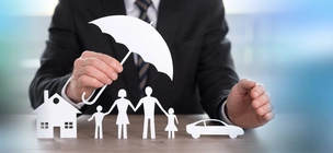 Agent osiguranja simbolično drži kišobran nad obitelji i njenom imovinom izrezanom iz papira.
