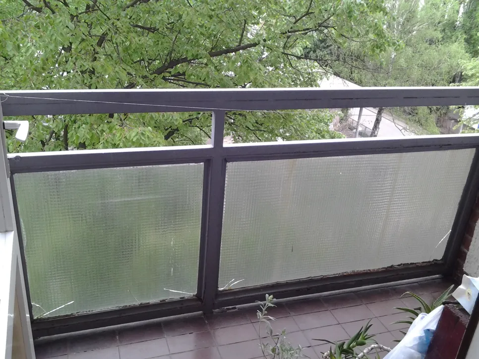 Oštećeni stakleni razdjelnik s pukotinama na balkonskoj ogradi koji treba pregledati zbog mogućih sigurnosnih problema.