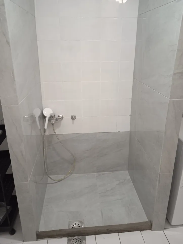 Shower with inadequate water drainage showing pooled water near the drain and uneven tiles.