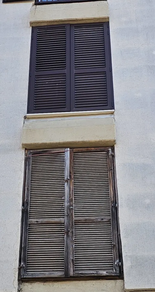 Worn and discolored window shutters on a building exterior showing signs of aging and weather exposure.