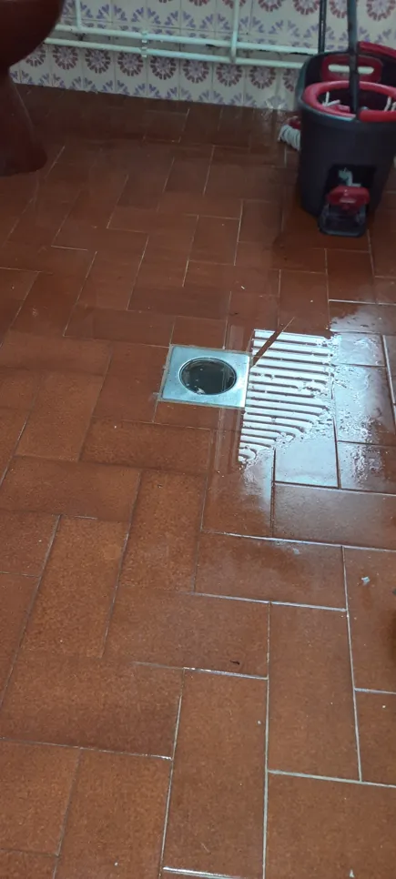 Water pooling on tiled bathroom floor indicates a drain blockage issue.