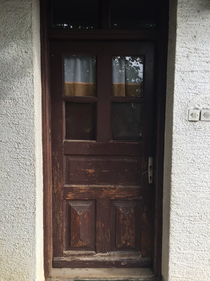 A distressed wooden door features peeling brown paint, revealing weathered wood beneath.