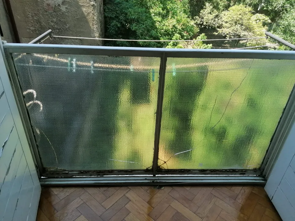 Puknuto staklo na ogradnom balkonu s drvećem vidljivim vani, ističući sigurnosne brige.