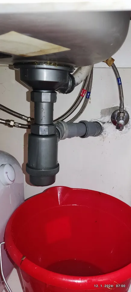 Propuštanje vodovodnih cijevi ispod sudopera s crvenom kanticom koja hvata vodu i vidljivim spojnicama cijevi.