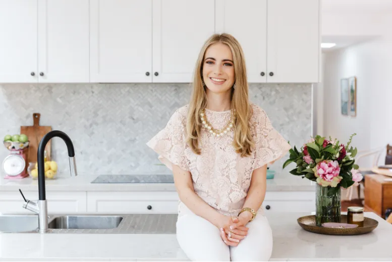 Dizajnerica interijera sjedi na pultu bijele kuhinje nakon dobro odrađenog posla.