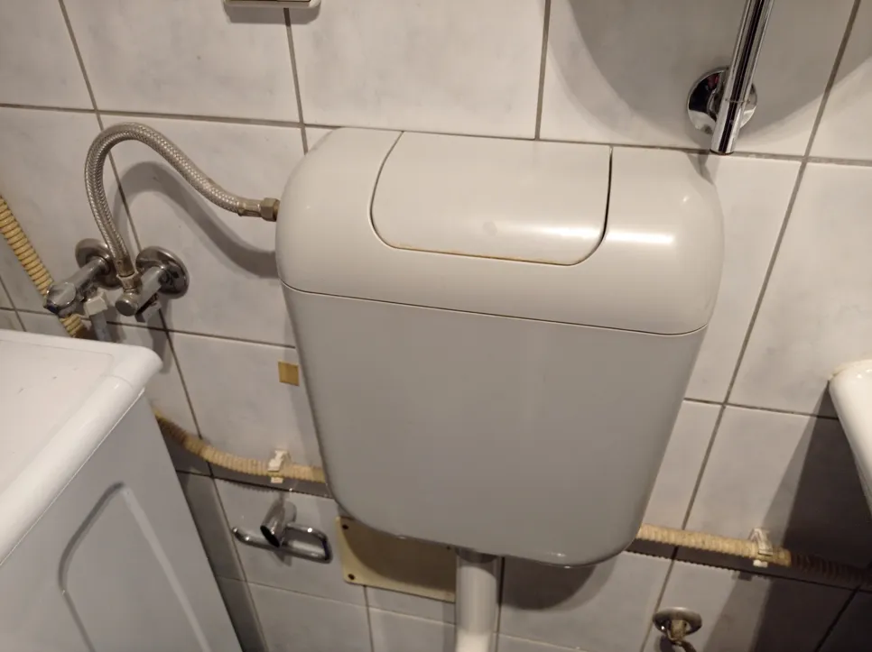 Cureća toaletna cisterna s vidljivim vodovodnim crijevima i spojnim elementima, što ukazuje na moguće curenje vode.