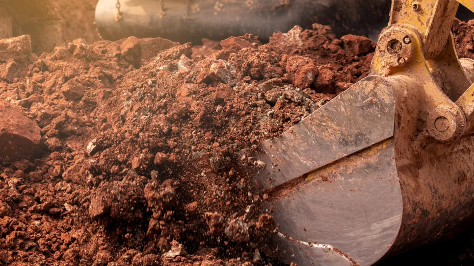 Prvi plan bagerove ruke pune crvene zemlje.