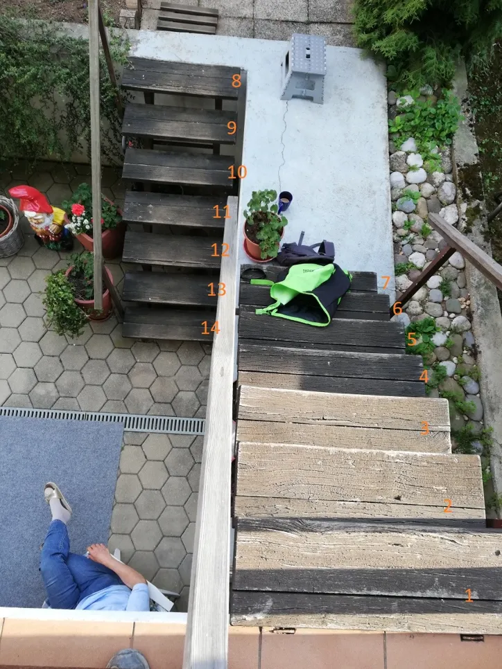 Pogled iz ptičje perspektive na drvenu vanjsku stepenicu s nejednako raspoređenim stepenicama, koja vodi do vrtnog prostora ispod.