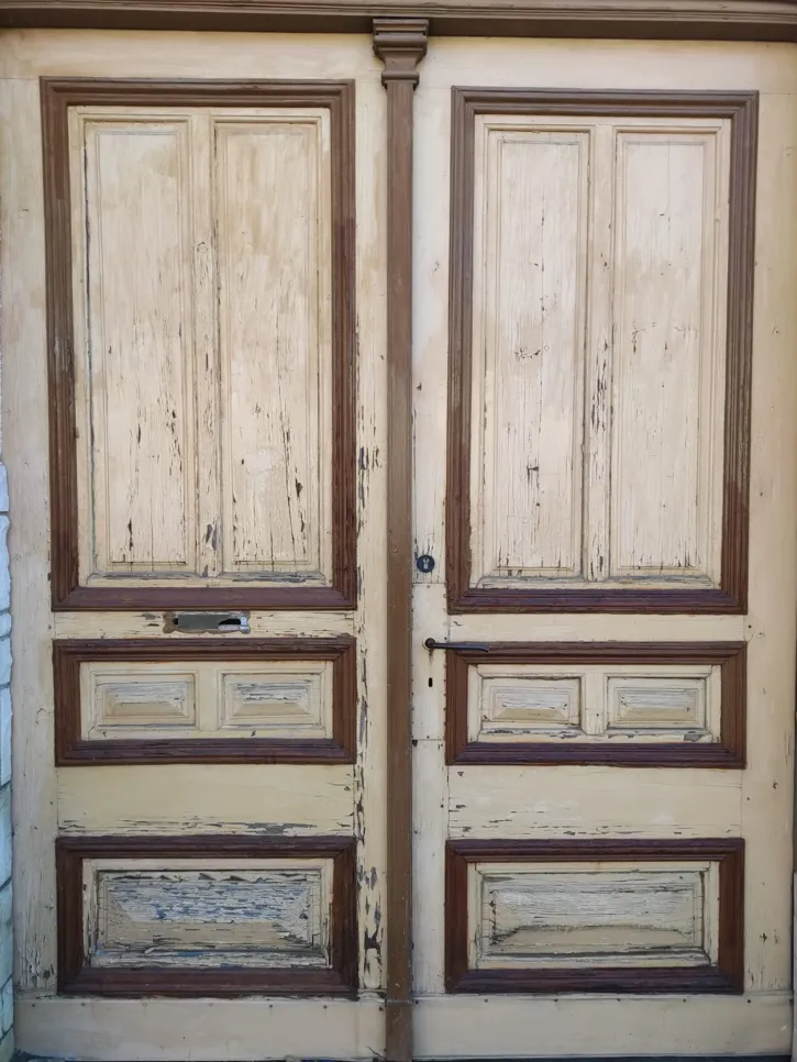 A pair of aged wooden doors with peeling paint and visible wear and tear, highlighting the need for restoration.