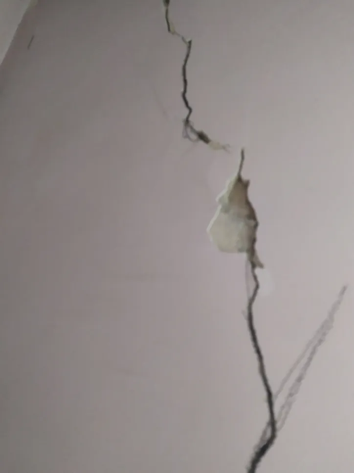 Close-up view of a large vertical crack in a plaster wall, indicating potential structural damage.