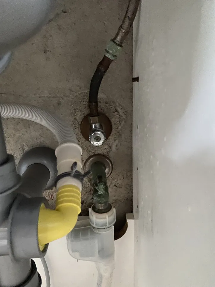 Korodirana spojna cijev u riziku od curenja ispod kuhinjskog sudopera, okružena odvodnim crijevima.