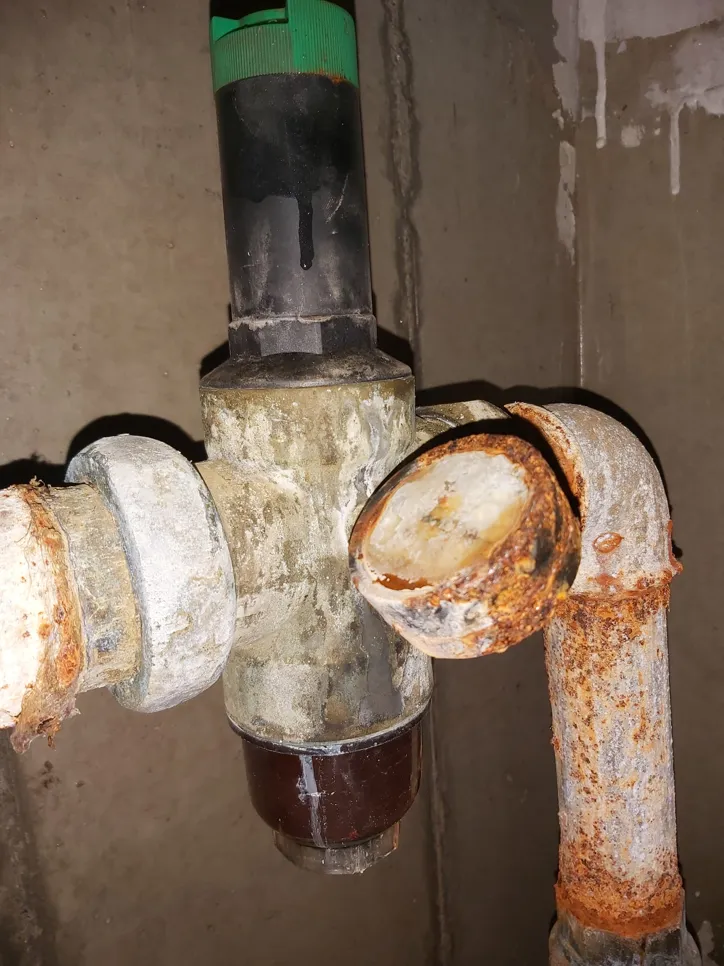Severely rusted water pipe and valve with visible corrosion, indicating potential leaks and plumbing issues.