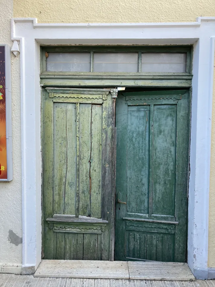 A faded and cracked wooden door displaying signs of age and weather damage, with peeling paint and wood deterioration.