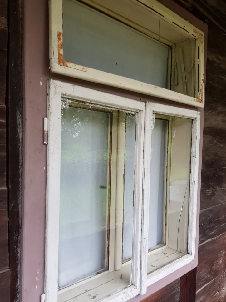 A wooden window frame with visible cracks and peeling paint, showing neglect and potential water damage.