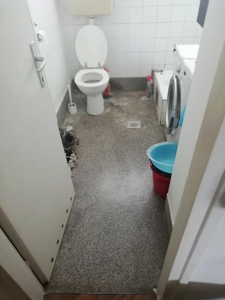 Small bathroom showing water accumulation near toilet indicating drainage issue.