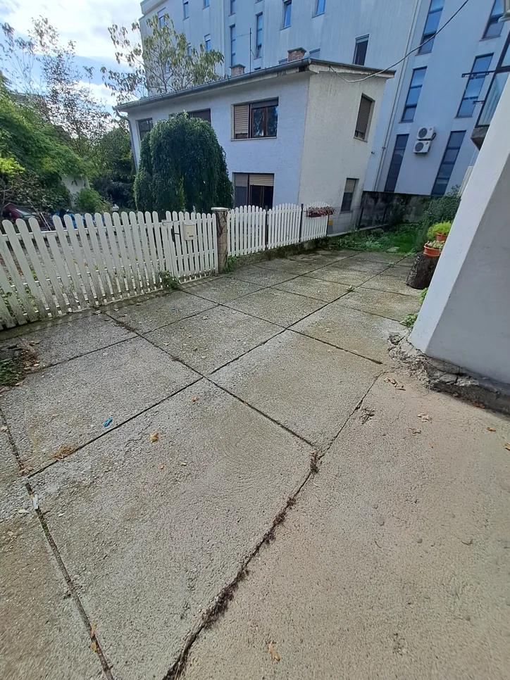 Concrete driveway with uneven surface and visible sloping sections, surrounded by a garden fence.
