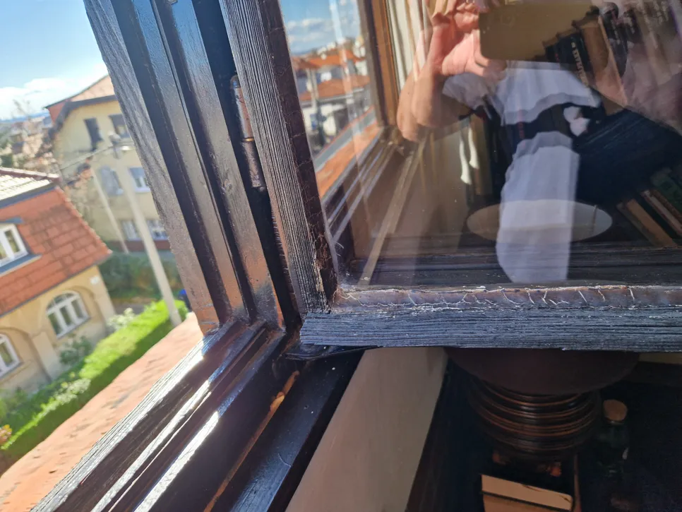 Old wooden window frame showing signs of peeling paint and dryness, indicating potential weather damage.