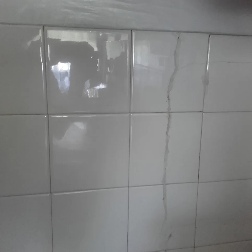 Puknuta bijela pločica u kupaonici s vidljivim vertikalnim pukotinama, što ukazuje na potencijalne probleme s vodom ili slaganjem.