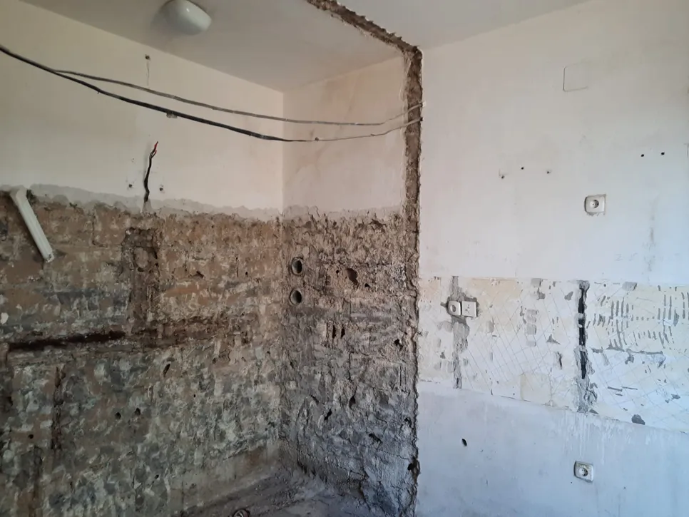 Nedovršeni zid s izloženim električnim kablovima i utičnicama, prikazujući sirovi malter i cijevi.