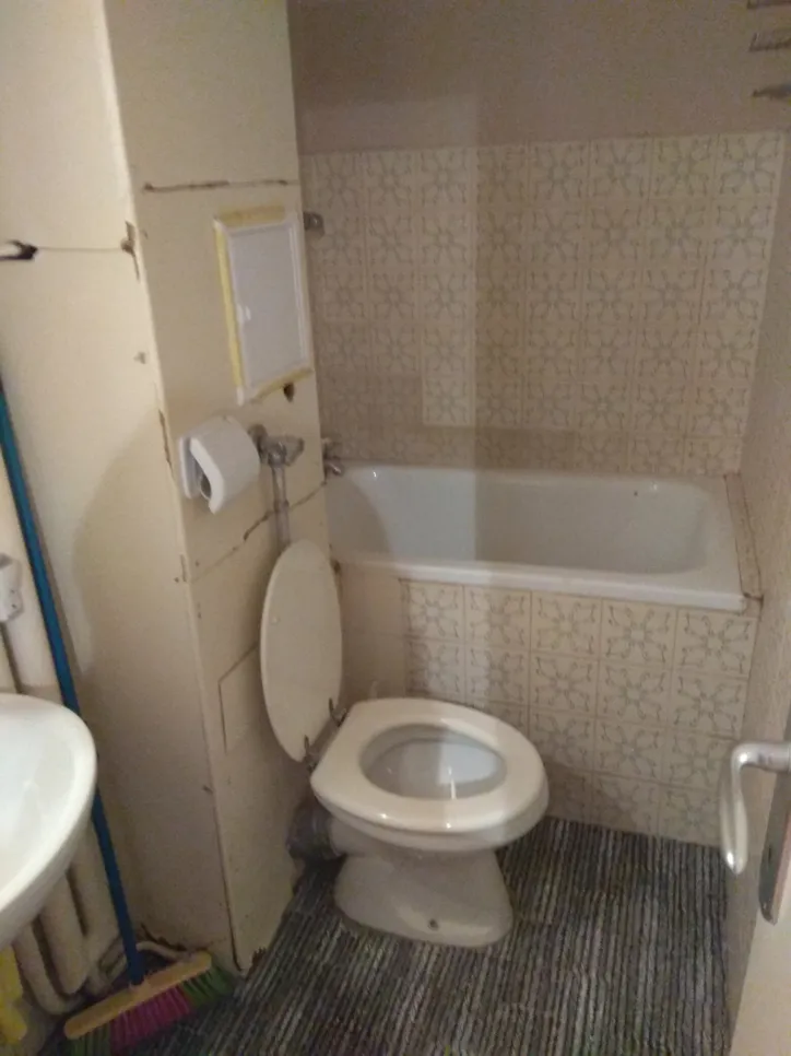 Small bathroom featuring a misplaced toilet positioned adjacent to a bathtub, highlighting space utilization issues.