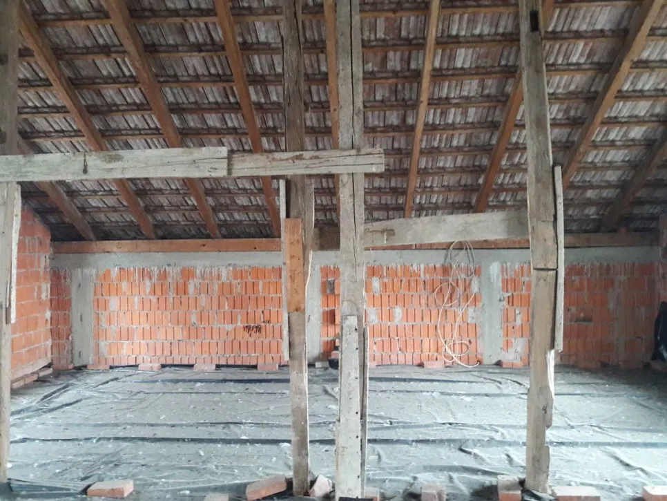 Nedovršeni prostor potkrovlja s izloženim drvenim gredama i zidovima od opeke spreman za renovaciju i izolaciju.