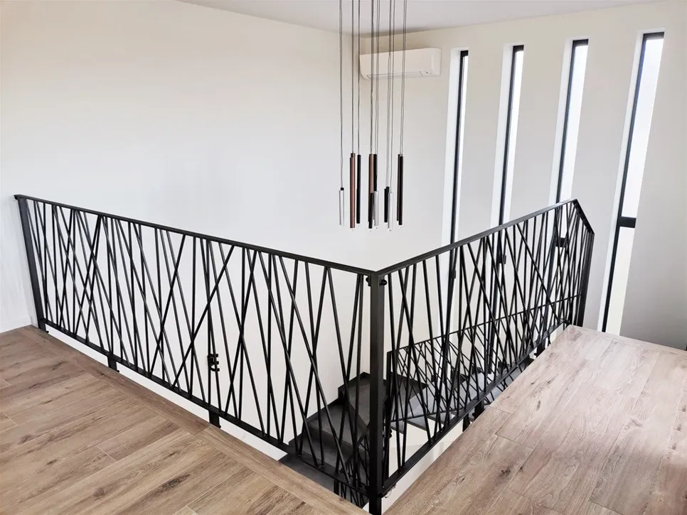 Elegantne crne metalne ograde s geometrijskim uzorkom poboljšavaju moderne stepenice, uz dodatak visećih svjetiljki.