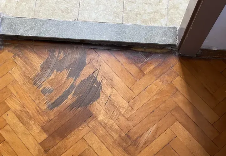 Mrlja od vode na drvenom podu u riblju kost stvara promjenu boje u blizini pragova pločica.