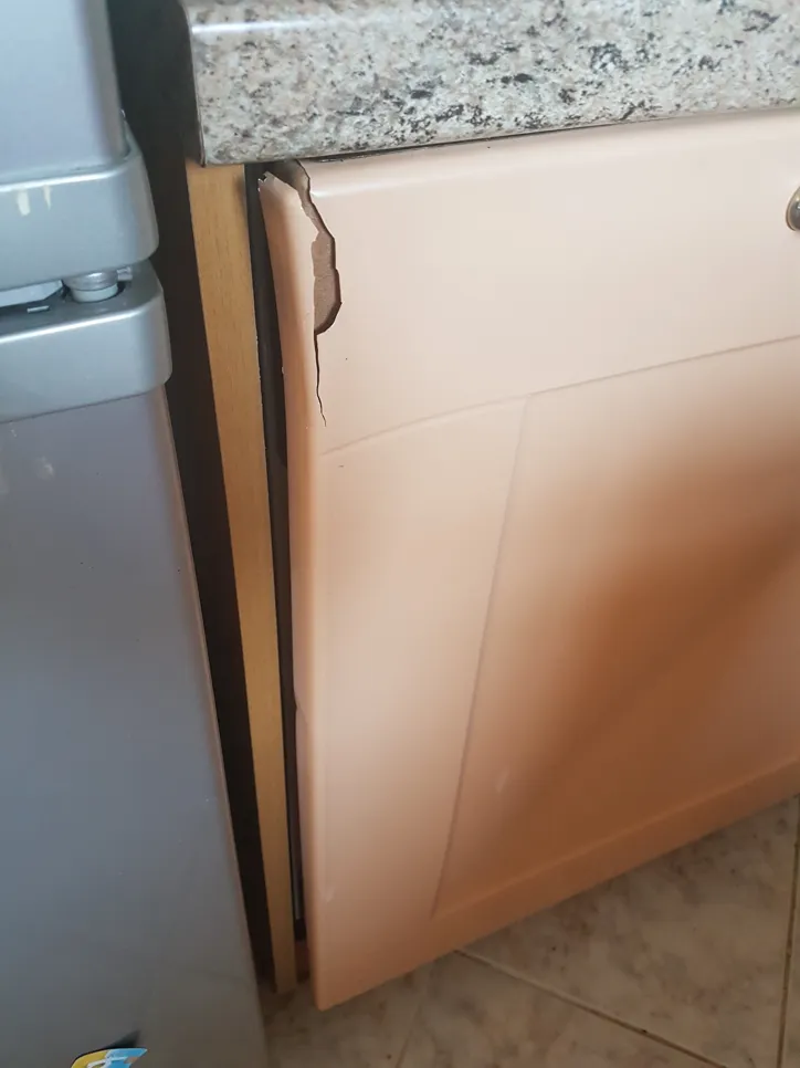 Puknuta vrata kuhinjskog ormarića pored granitne radne površine u kuhinjskom okruženju.