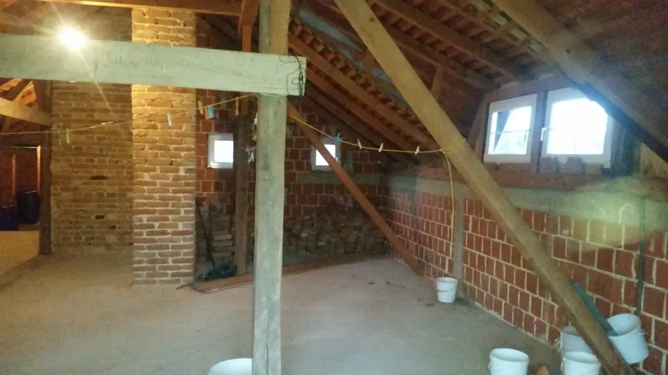 Nedovršeni potkrovni prostor s izloženim zidovima od opeke i drvenim gredama, pružajući rustičan, prostran izgled.