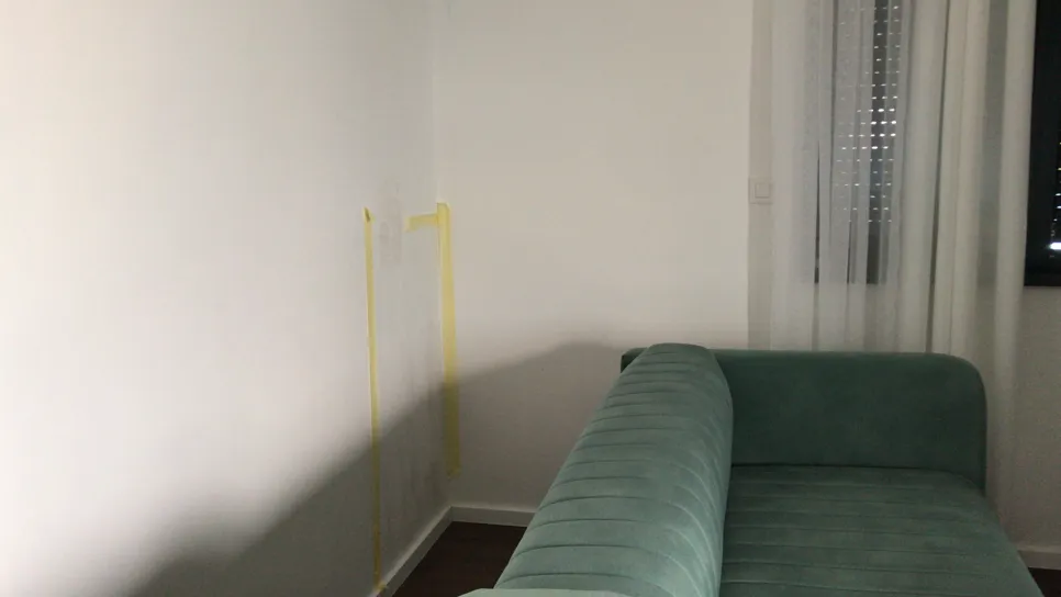 Dezoloracija plijesni na zidu iza kauča Bijeli zid s žućkastim mrljama plijesni iza plavog kauča, što ukazuje na moguće probleme s vlagom.