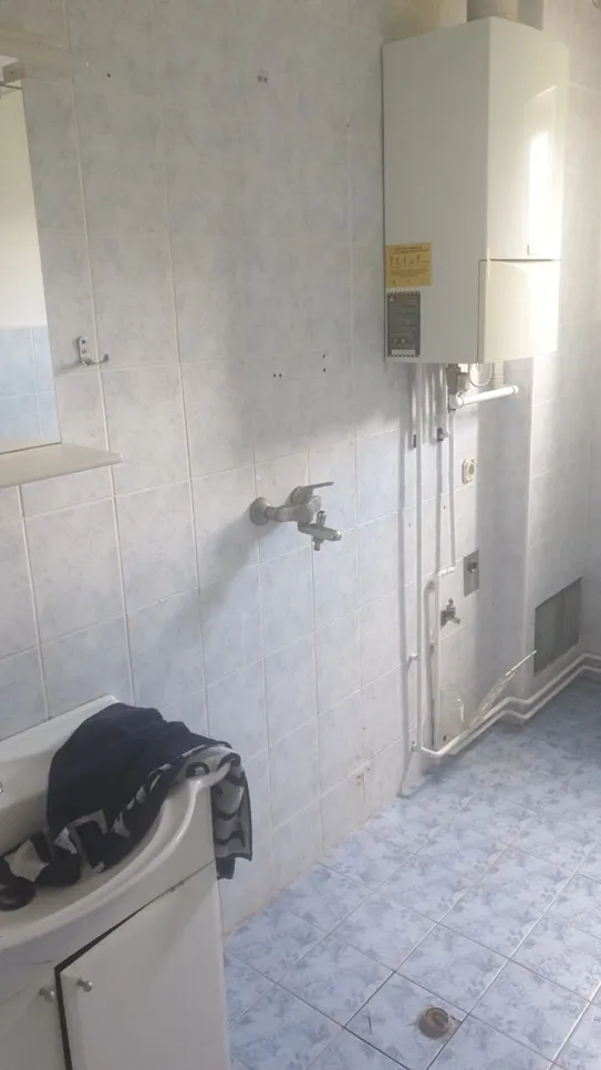 Kupaonica s zidnim bojlerom, pločicama na zidovima i vidljivim vodovodom.