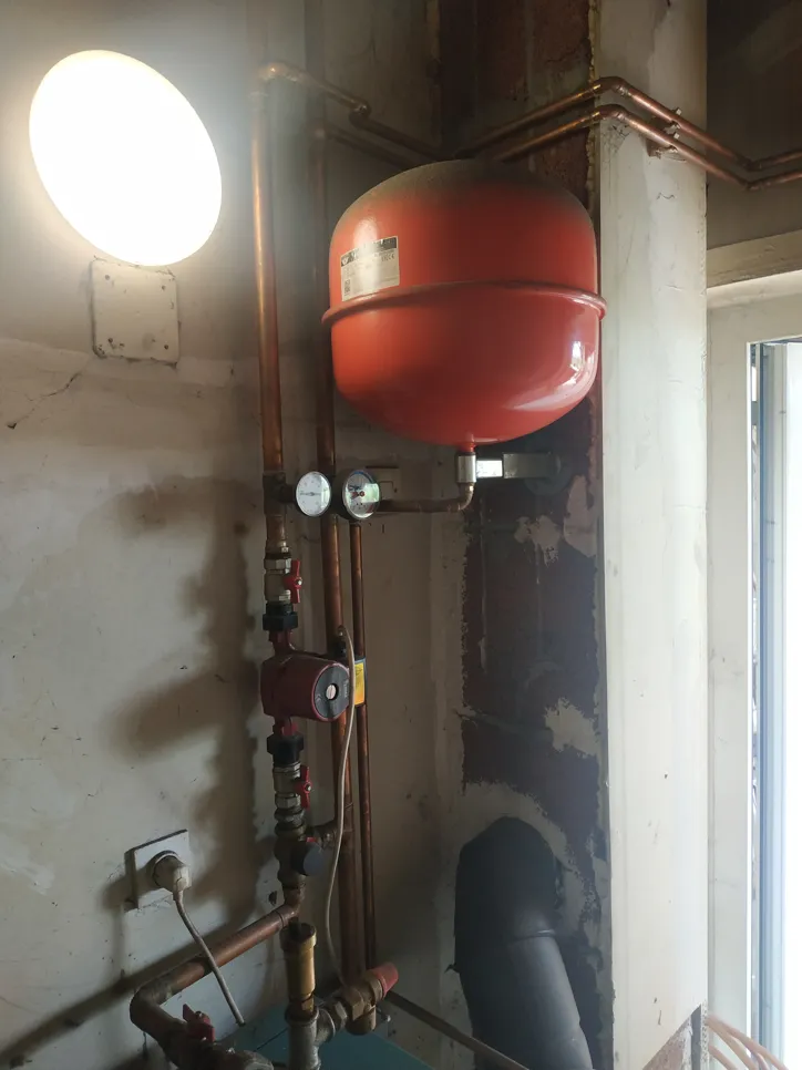 Zidno montirani sustav bojlera s crvenom ekspanzijskom posudom i bakrenim cijevima, s manometrom i ventilima.