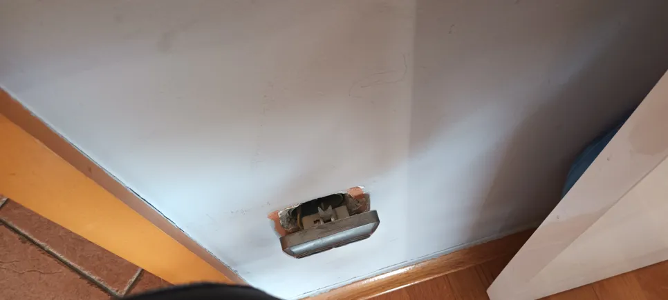 Izložena električna utičnica bez poklopca koja prikazuje žice na bijelom zidu blizu poda.