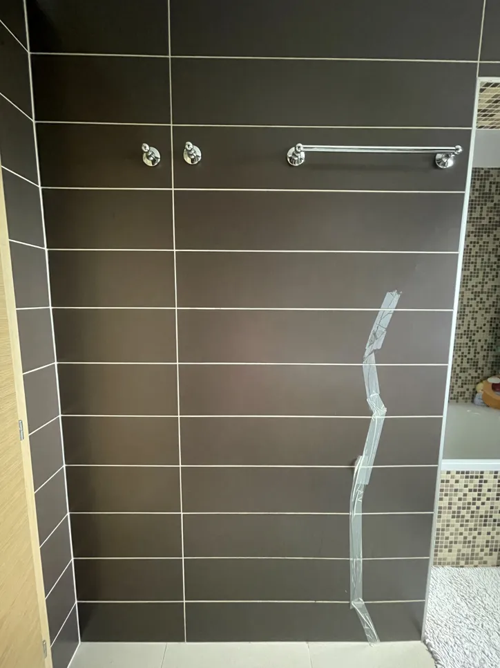 Pločice na zidovima kupaonice s vidljivom pukotinom osigurane trakama, ističući potencijalnu strukturnu zabrinutost.