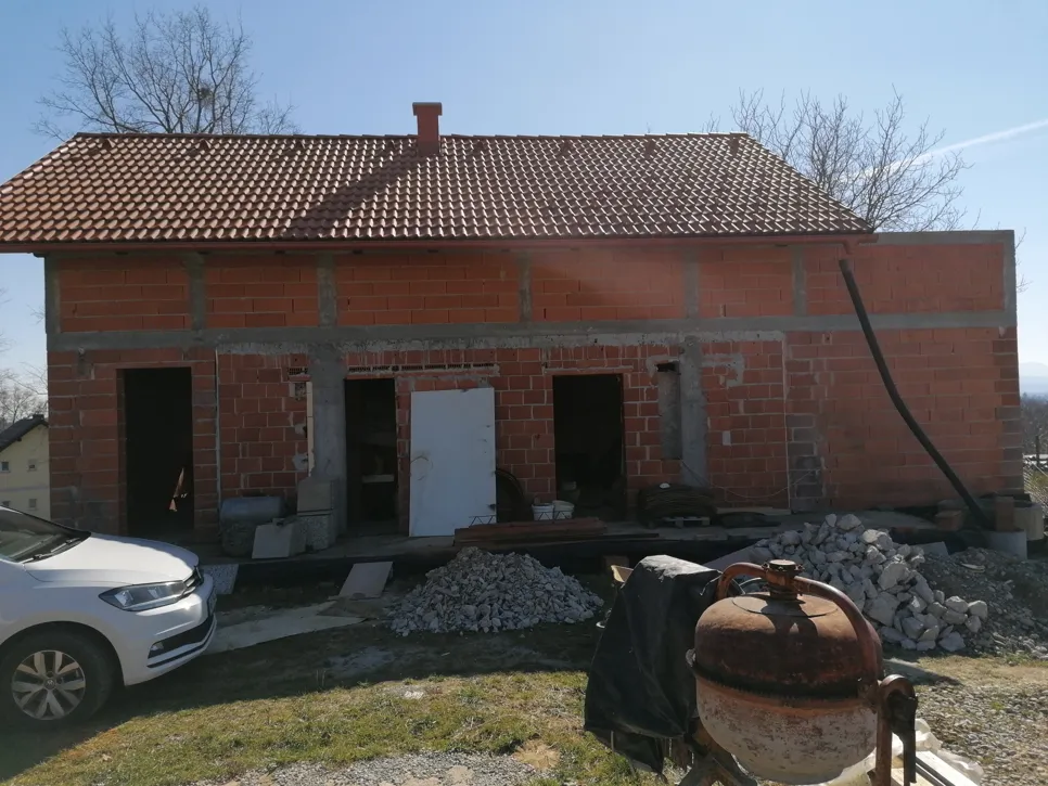 Nedovršena kuća od opeke s izloženim zidovima i krovnim pločicama, koja zahtijeva daljnje strukturno dovršenje.