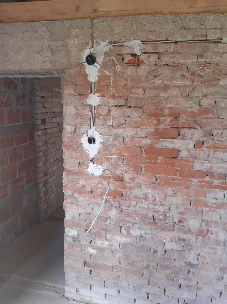 Izložena električna instalacija na zidnoj opeki koja ukazuje na nepotpunu instalaciju. Kablovi i kutije za utičnice su vidljive.