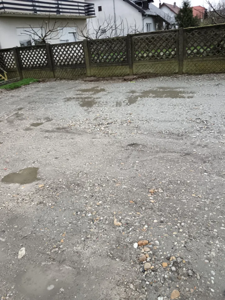 Unpaved gravel driveway with noticeable puddles and uneven surface near residential area.