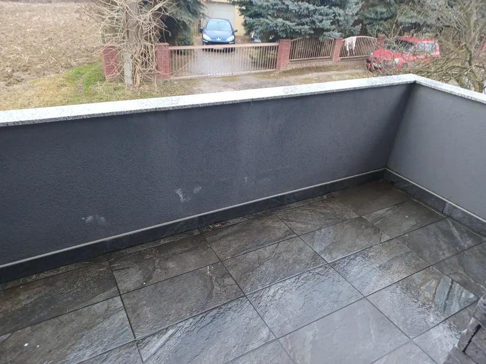 Wet gray tiles on a balcony surrounded by walls show potential drainage issues after rainfall.