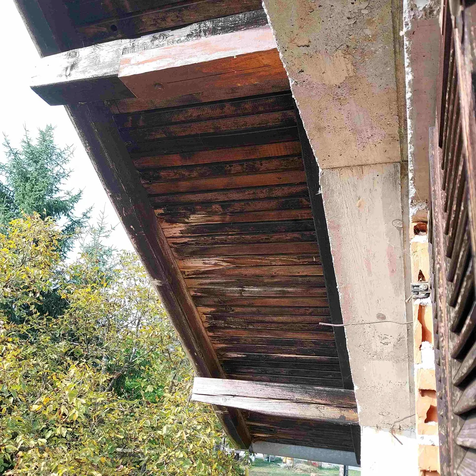 Ostarjeli drveni stropni rub izložen elementima, pokazuje znakove oštećenja i starenja.