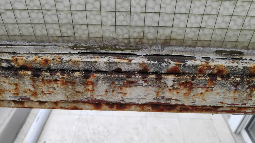 Teško hrđavi okvir prozora s ljuštenjem boje što ukazuje na naprednu koroziju metala.