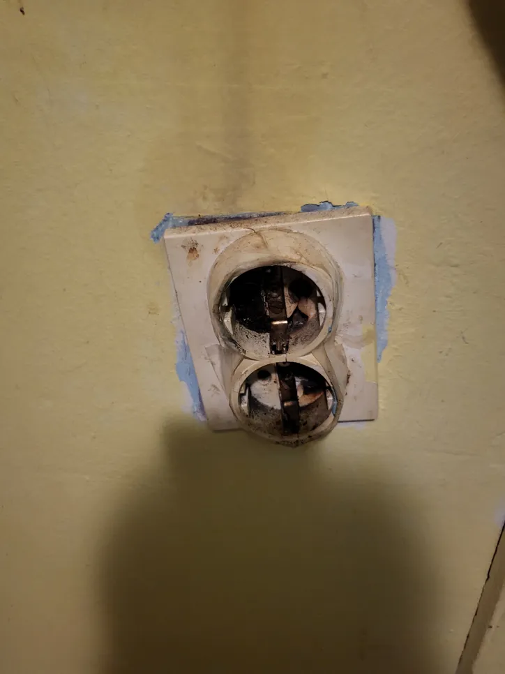 Slomljena i izložena električna utičnica na prljavom zidu, koja pokazuje znakove oštećenja i zapuštenosti.