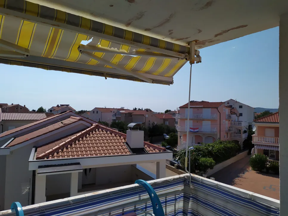 Nadstrešnica na balkonu sa žutim prugama koja pokazuje uočljive suze i trošenje.