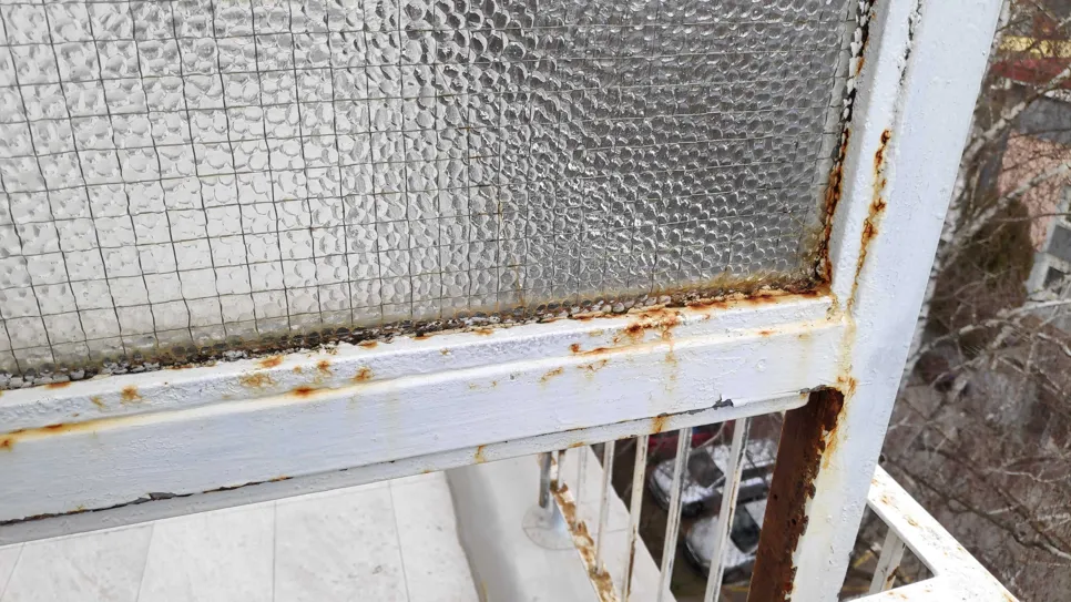 Hrđa se formira na bijelom metalnom okviru prozora, uzrokujući promjenu boje i potencijalne strukturne probleme.