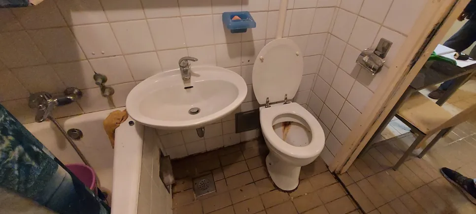 Compact bathroom featuring a sink and toilet in close proximity, highlighting limited space and clutter.