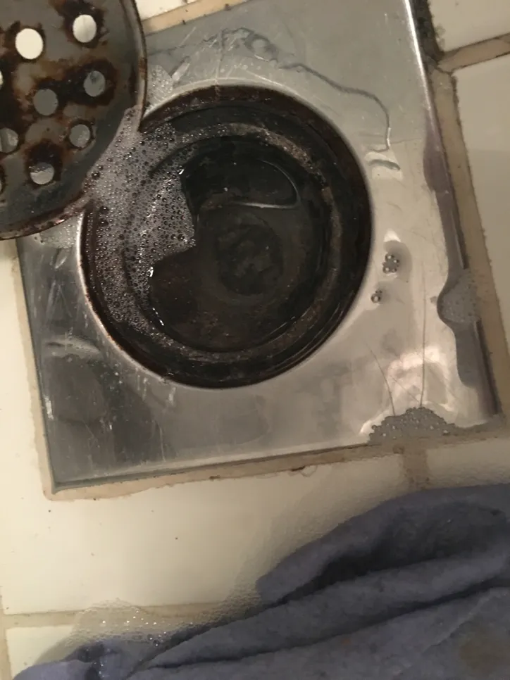 Tuš od nehrđajućeg čelika ispunjen stajaćom vodom, što ukazuje na mogući problem sa začepljenjem ili blokadom.