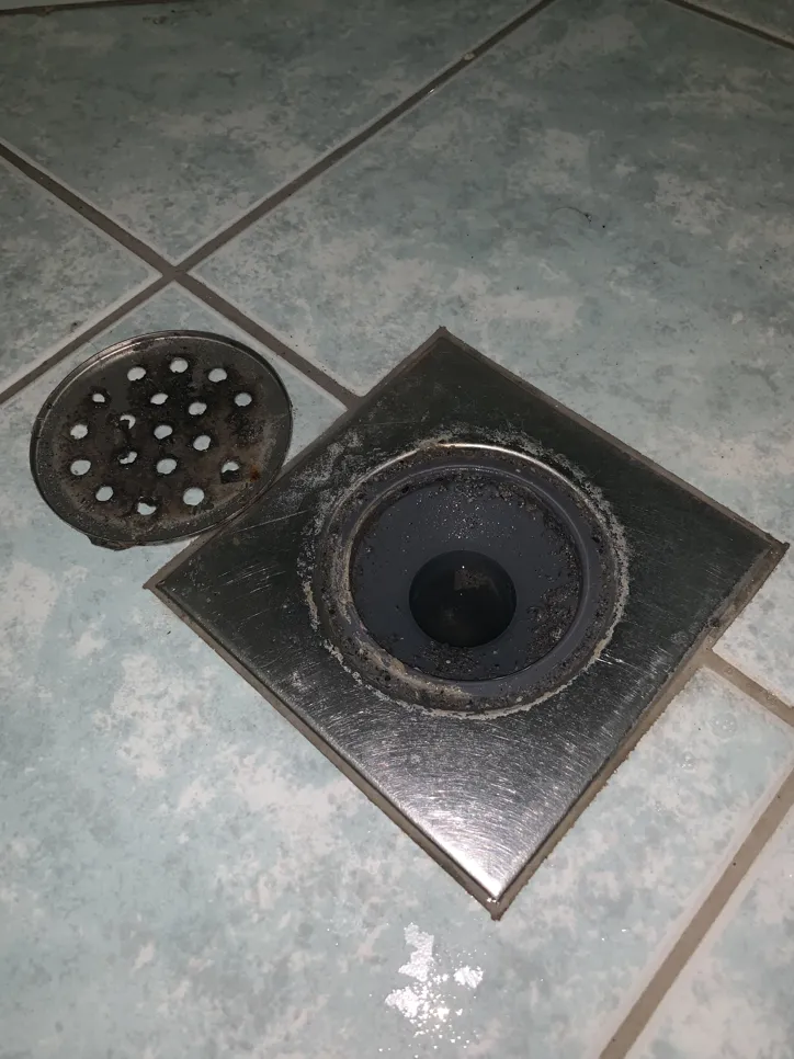 Pod tuša s otvorenim odvodom koji prikazuje nakupljanje otpada koje uzrokuje potencijalne probleme sa začepljenjem.