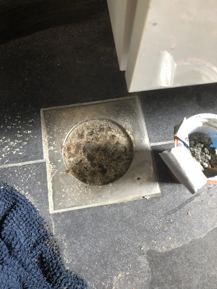 Prljavi odvod za tuš s vidljivim naslagama prljavštine i otpada koji uzrokuju blokadu na pločicama kupaonice.