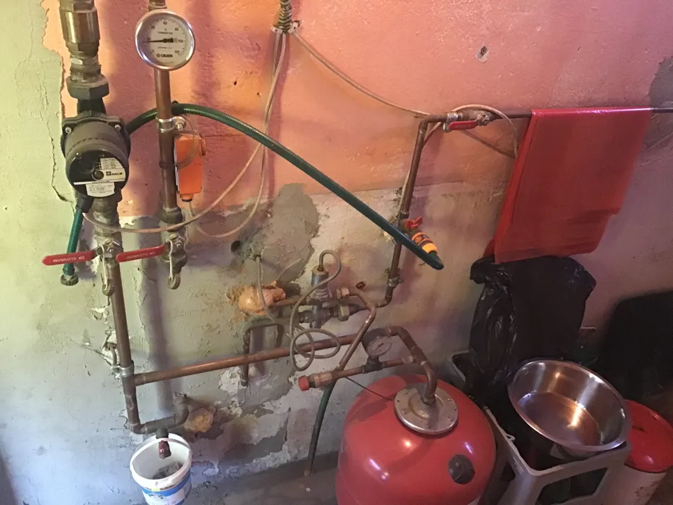 Stambeni sustav grijanja s cijevima, manometrima i crvenom ekspanzionom posudom vidljivom uz zid.