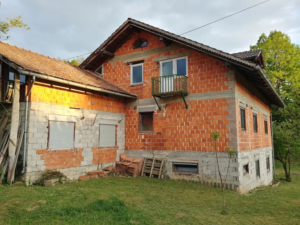 Djelomično izgrađena kuća od opeke s otkrivenom vanjštinom koja prikazuje nedovršene zidove i okvire prozora.