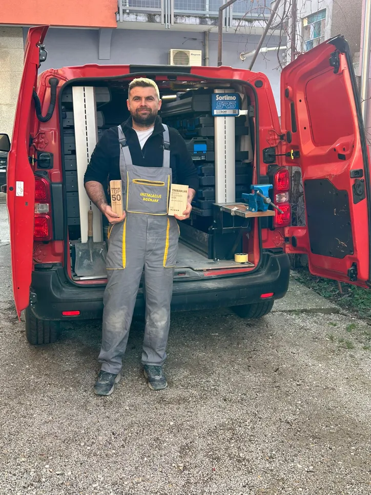 Vlasnik tvrtke Instalacije Bošnjak ispred svog radnog vozila, držeći priznanja Trebam.hr TOP 50 i Odabir klijenata 2025., zaslužena uz maksimalnu ocjenu 5.0.